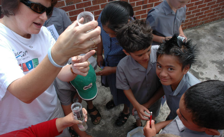 Photo of teacher Sally Smith showing a water sample to children.